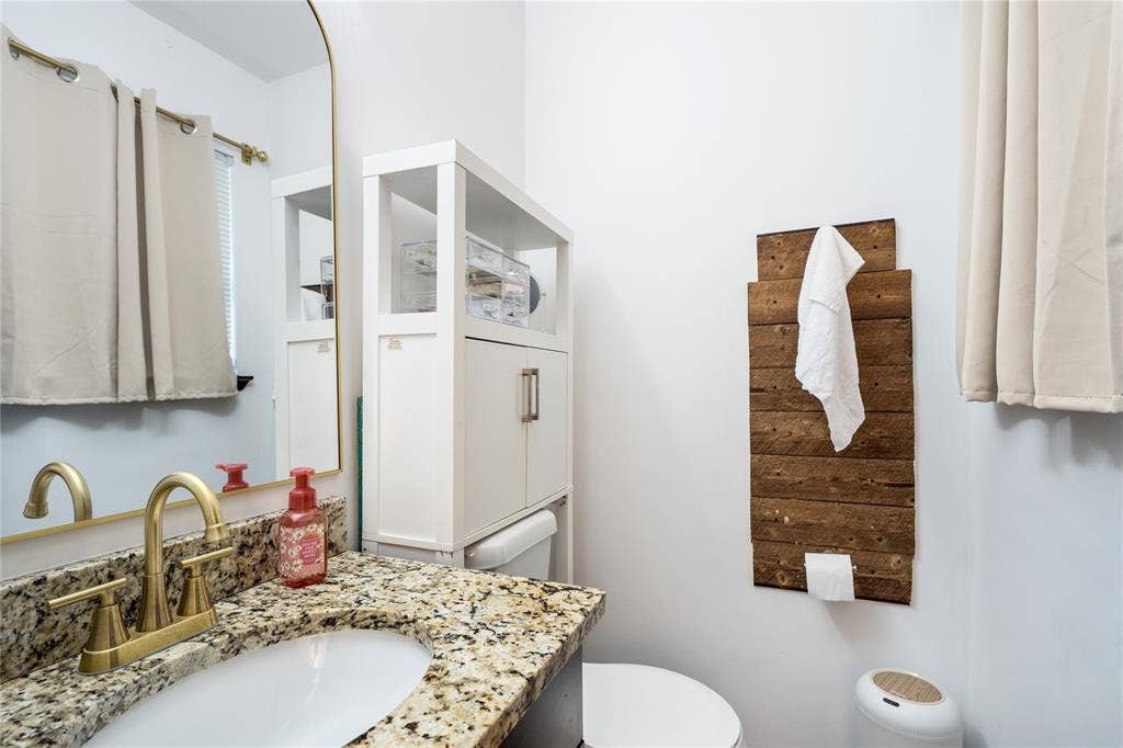 Bathroom featuring a stone countertop with an undermount sink, a brass-finish dual-handle faucet, and an arched wall mirror