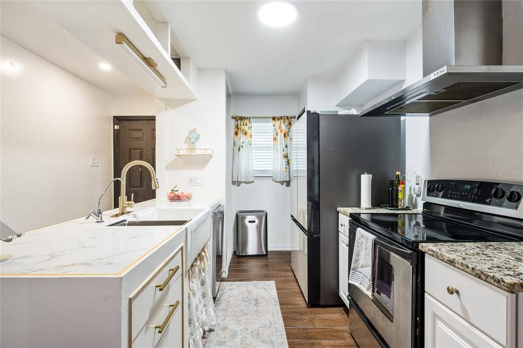 Kitchen featuring an apron-front sink, gold-tone faucet, stone-surfaced countertops, stainless steel appliances, and wood-finish flooring