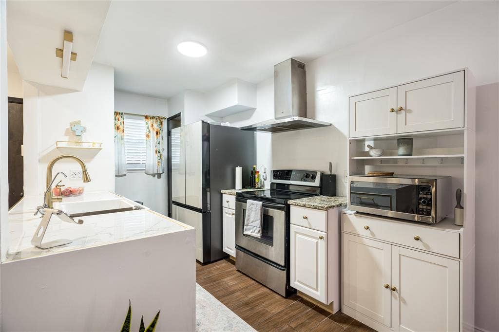 Kitchen featuring wood-finish flooring, white cabinetry, stone-patterned countertops, a stainless steel chimney-style range hood, and a high-arch faucet
