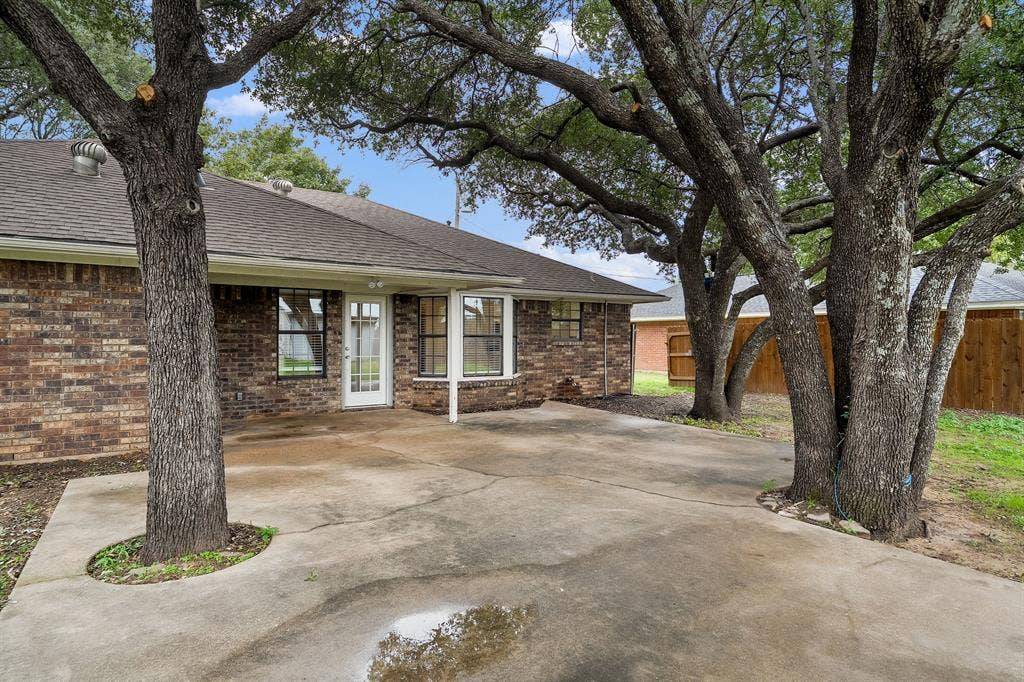 4043 Country Meadows Circle, Granbury, TX 76049 Brick exterior with a concrete patio, mature trees, and wood-paneled fencing