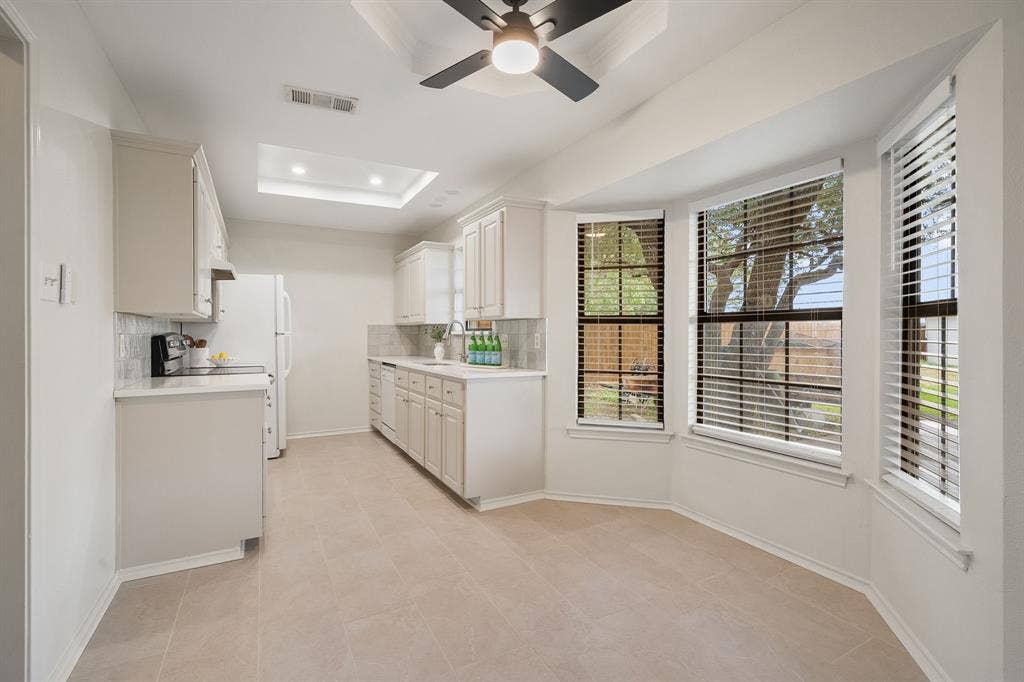 4043 Country Meadows Circle, Granbury, TX 76049 Kitchen featuring neutral cabinetry, quartz countertops, tile flooring, tray ceiling with integrated lighting, and dining area with a bay window
