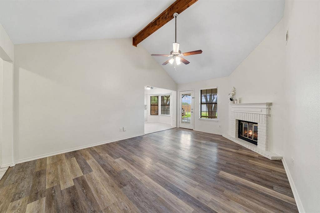 4043 Country Meadows Circle, Granbury, TX 76049 Vaulted ceiling featuring a prominent wooden support beam, LVP flooring, white brick fireplace with a mantel, and a ceiling fan with integrated lighting