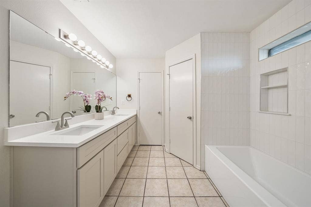 4043 Country Meadows Circle, Granbury, TX 76049 Bathroom featuring an expansive vanity with dual undermount sinks, solid-surface countertop, full-width mirror, tile flooring, and a tub-shower combination with built-in wall shelving
