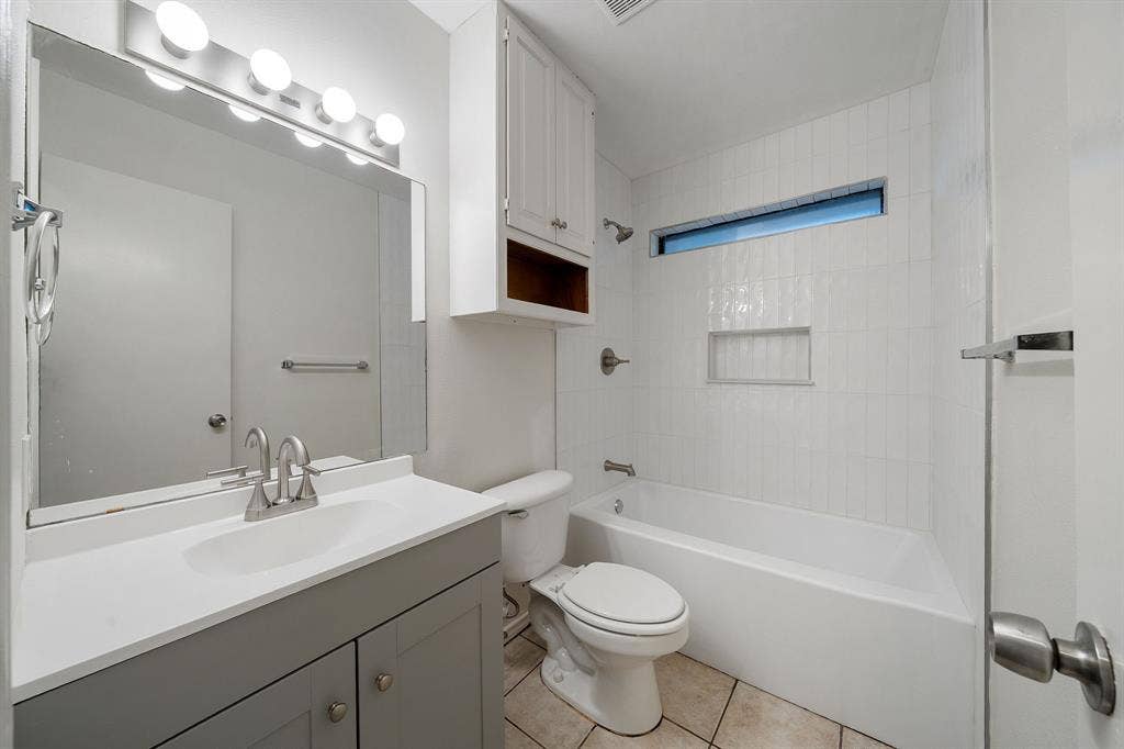 4043 Country Meadows Circle, Granbury, TX 76049 Bathroom featuring a grey vanity with a solid-surface countertop, white tile tub surround with a built-in niche, clerestory window, and over-mirror light fixture