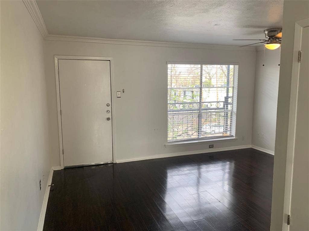 Dark wood-finish flooring, neutral walls, crown molding, a multi-pane window with installed blinds, and a ceiling fan with integrated lighting
