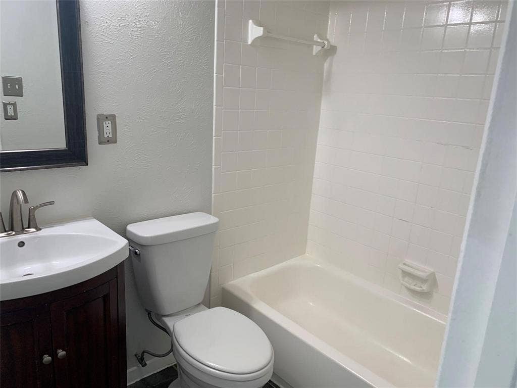 Bathroom featuring a dark wood-finish vanity, white basin sink with a curved faucet, white tile shower surround, and integrated soap dish