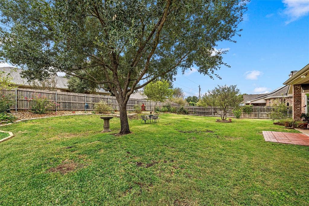 Backyard featuring a grass lawn, mature trees, wood privacy fencing, stone landscape edging, and a brick paver patio