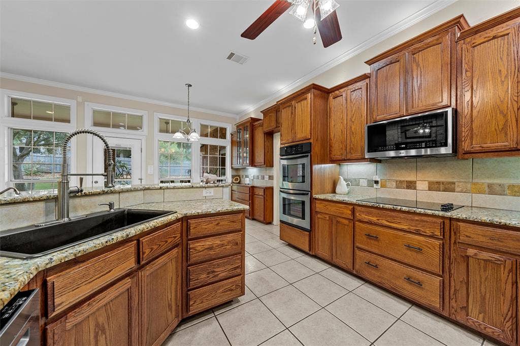 Kitchen featuring stained wood cabinetry, stone countertops, stainless steel double wall ovens, built-in microwave, and tile flooring