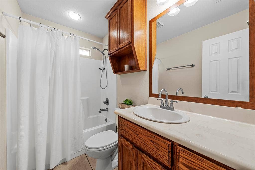 Bathroom featuring a wood vanity, an integrated countertop with an oval sink, a wall-mounted storage cabinet, and a shower-tub combination