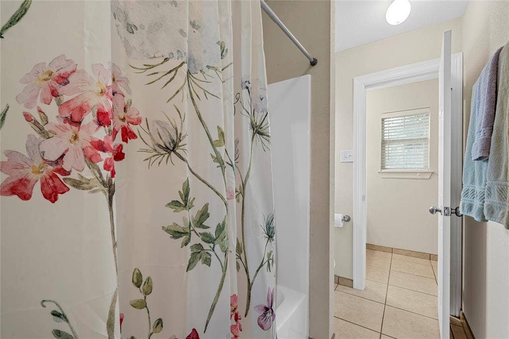 Bathroom featuring a composite shower surround, tile flooring, and a window with horizontal blinds
