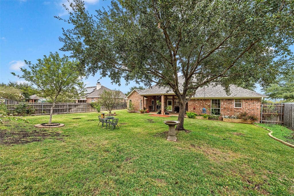 Expansive backyard featuring a brick exterior, covered patio, mature trees, and wood privacy fencing