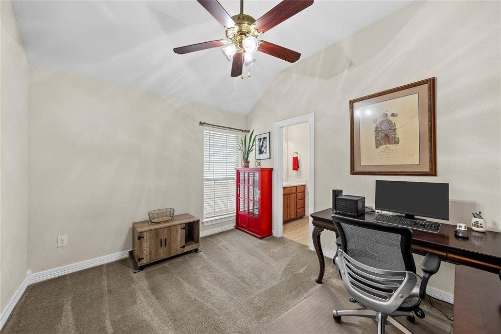 Vaulted ceiling featuring a central multi-blade ceiling fan with integrated light fixture, neutral wall palette, carpeting, and a single window with slatted blinds