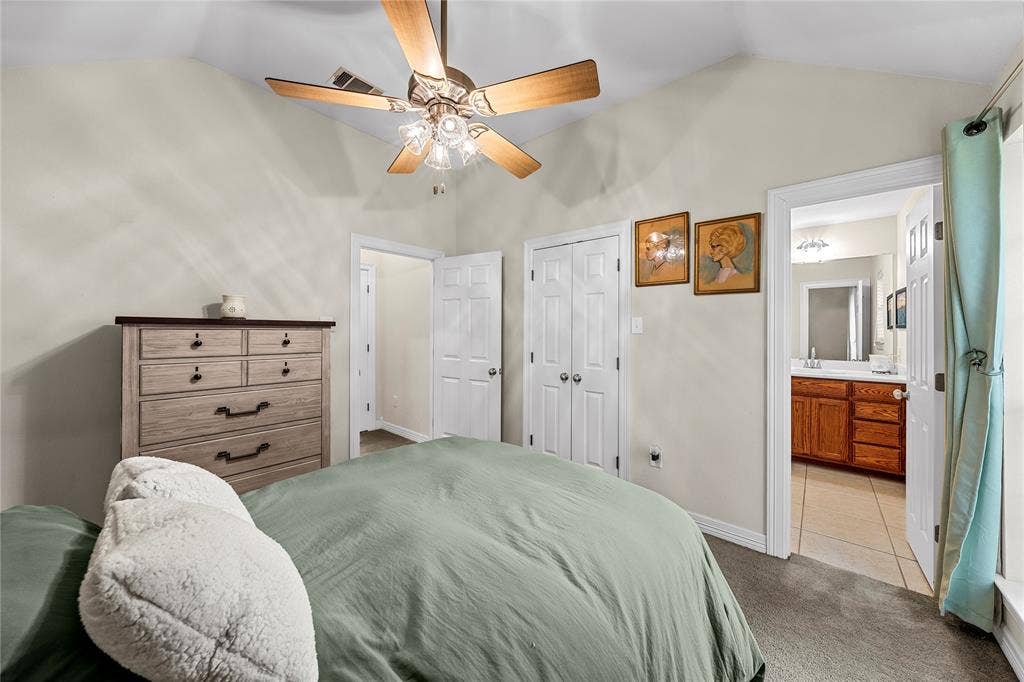 Vaulted ceiling, multi-blade ceiling fan with integrated lighting, dual-panel closet doors, and wood-finish cabinetry