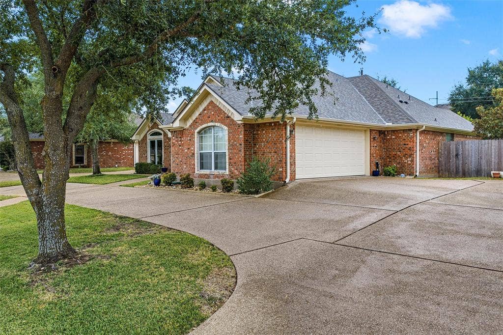 Single-story brick exterior with a gabled roofline, multi-car garage, expansive concrete driveway, and mature landscaping