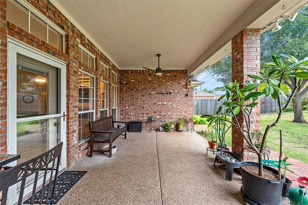 Covered patio featuring exposed brick exterior walls, a concrete floor, integrated ceiling fan, and large windows with transom accents