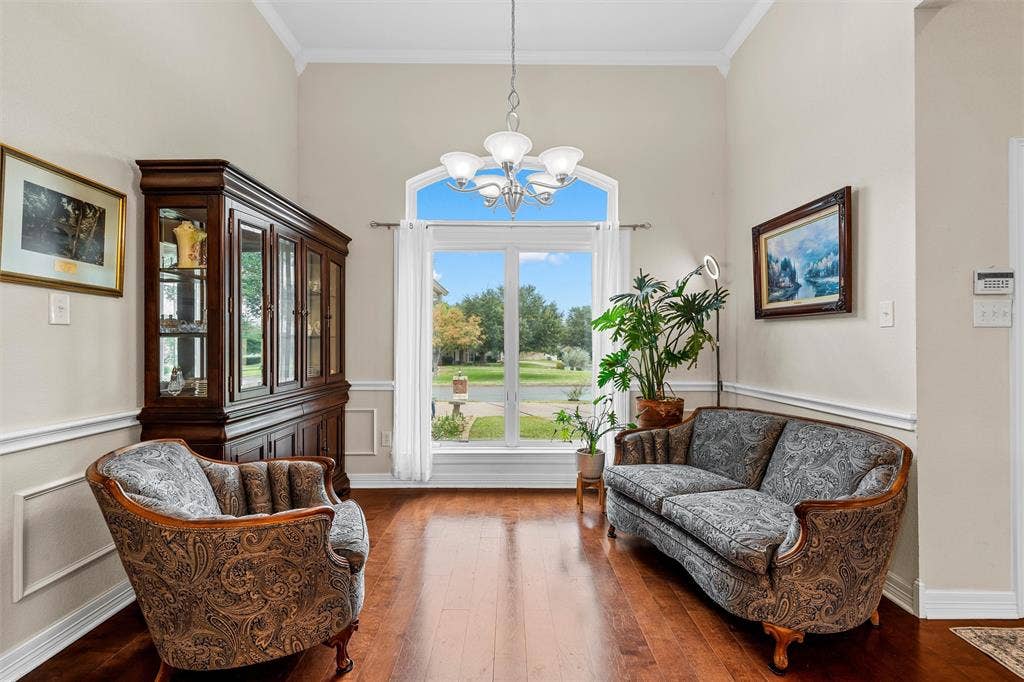 High-ceilinged room featuring wood-finish flooring, wainscoting, a multi-light chandelier, and an arched window