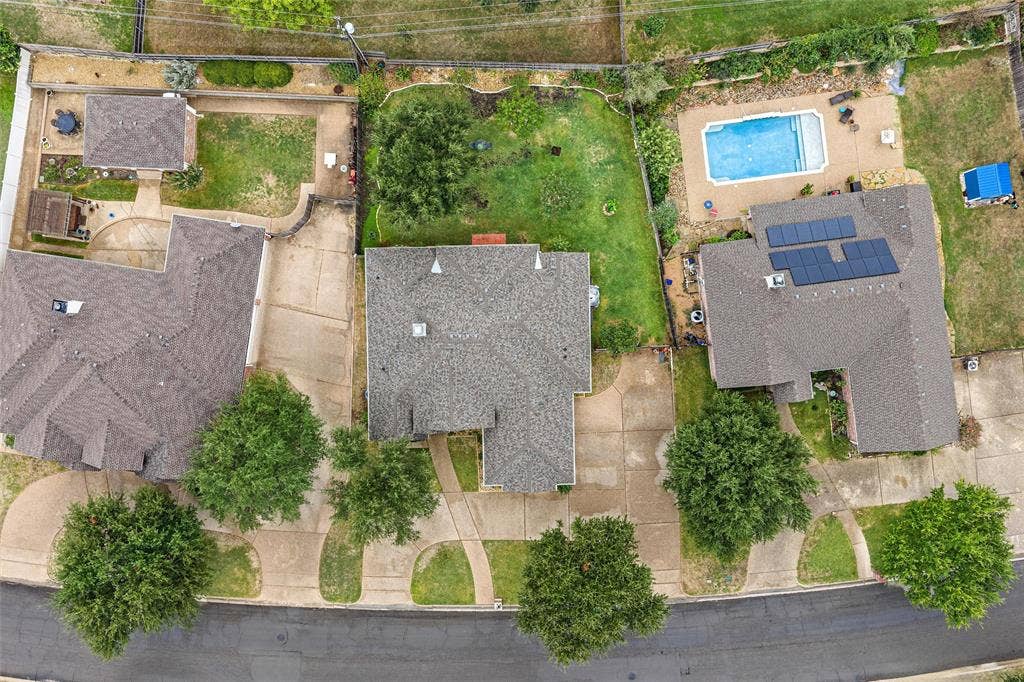 Aerial perspective featuring multiple residential lots with concrete driveways, mature trees, expansive lawns, and private in-ground swimming pool