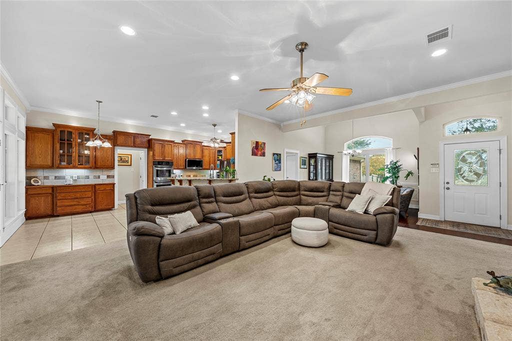 Open-concept interior featuring light-toned carpeting, recessed lighting, ceiling fans with integrated light fixtures, kitchen with wood cabinetry, and an exterior door with decorative glass paneling