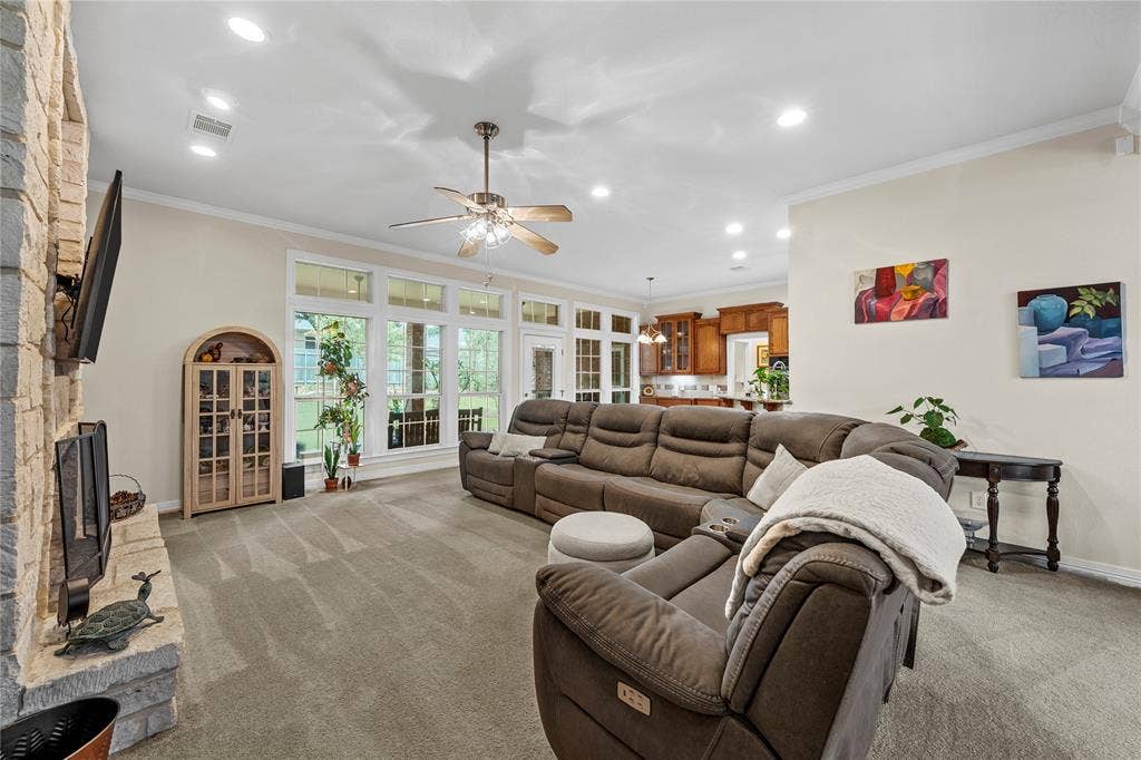 Floor-to-ceiling stone fireplace, series of large multi-pane windows, recessed ceiling lighting, ceiling fan with integrated light fixture, and arched built-in cabinetry