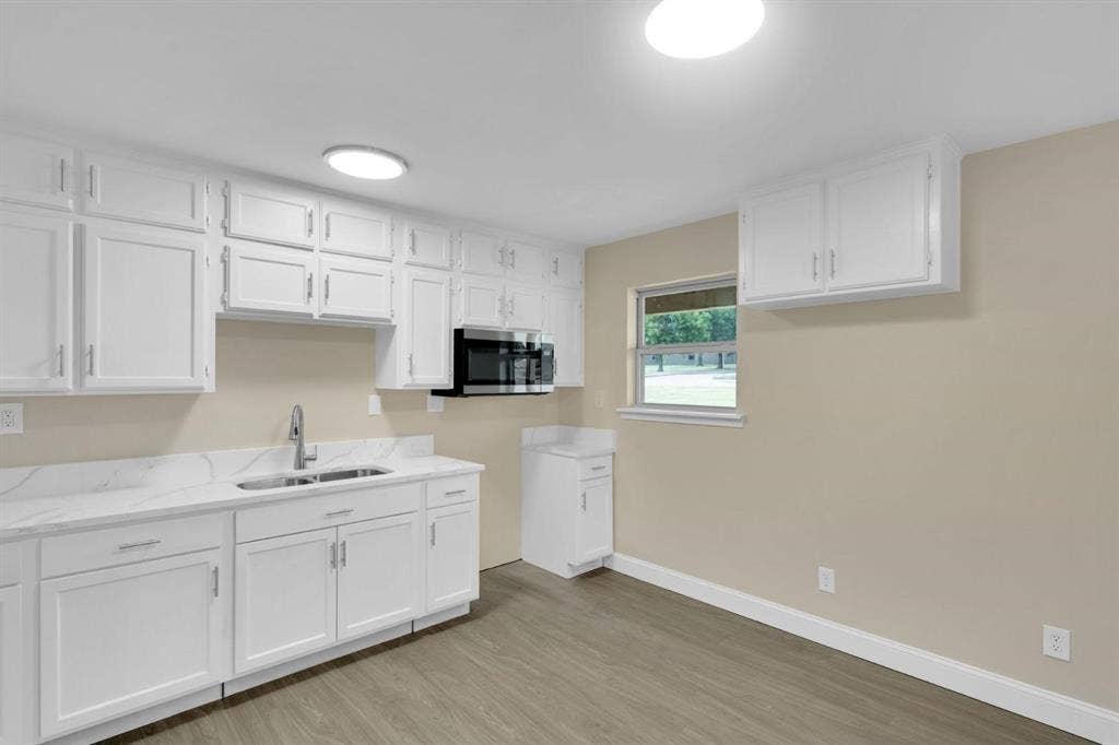 705 George Hopper Road, Midlothian, TX 76065 Kitchen featuring white cabinetry, stone-finish countertops, an integrated microwave, a double-basin stainless steel sink with a high-arch faucet, and wood-finish flooring