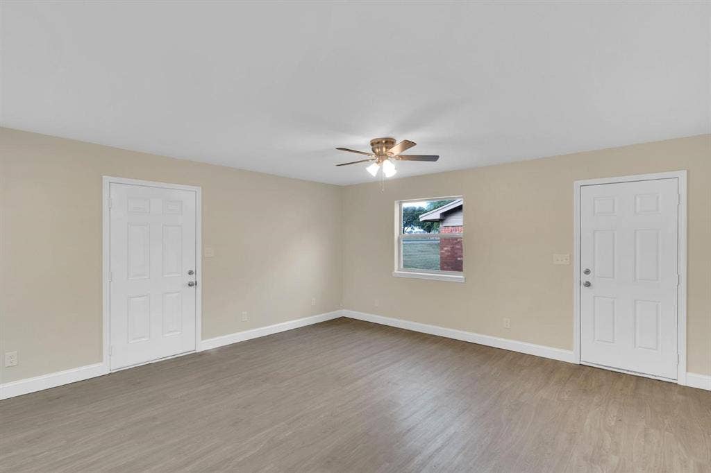 705 George Hopper Road, Midlothian, TX 76065 Neutral-toned interior space featuring wood-finish flooring, a ceiling fan with integrated lighting, two six-panel doors, and a single-pane window