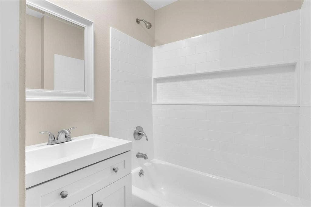 705 George Hopper Road, Midlothian, TX 76065 White vanity with a rectangular sink, brushed nickel dual-handle faucet, framed wall mirror, and tub-shower combination featuring white tile surround with a built-in recessed shelf