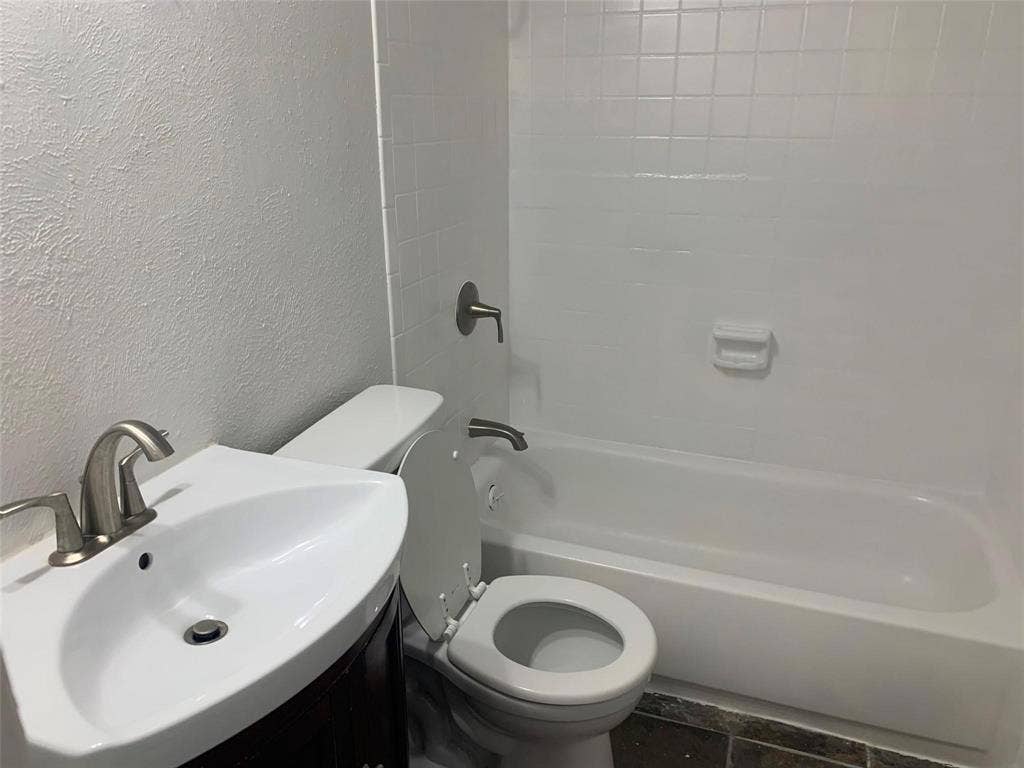 Bathroom featuring a white pedestal sink with a metallic faucet, a porcelain-surround shower and tub combination with a built-in soap dish, and dark tiled flooring