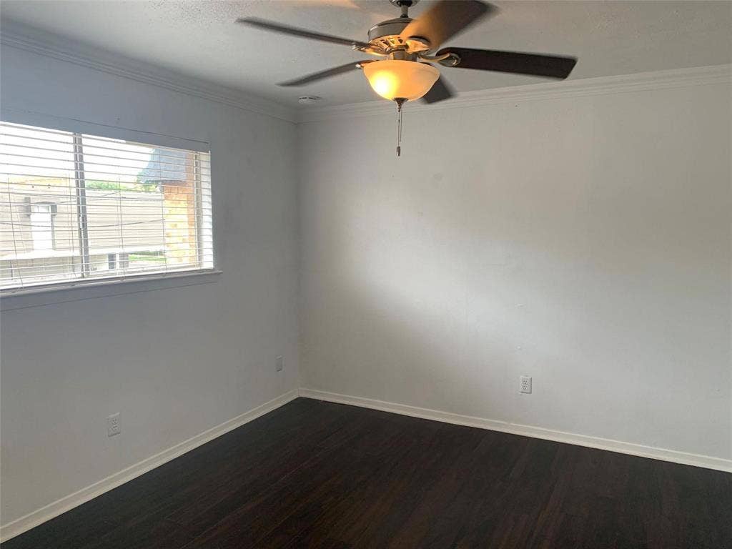 Room featuring dark wood-finish flooring, white walls, crown molding, horizontal blinds, and a ceiling fan with integrated lighting
