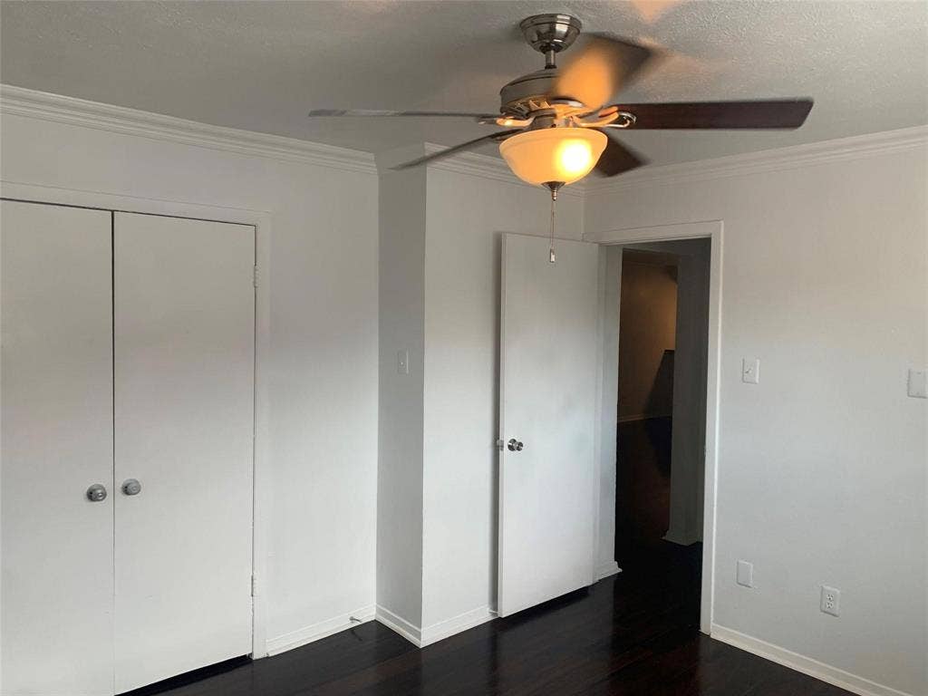 Dark-toned wood-finish flooring, crown molding, double-door reach-in closet, and ceiling fan with integrated lighting