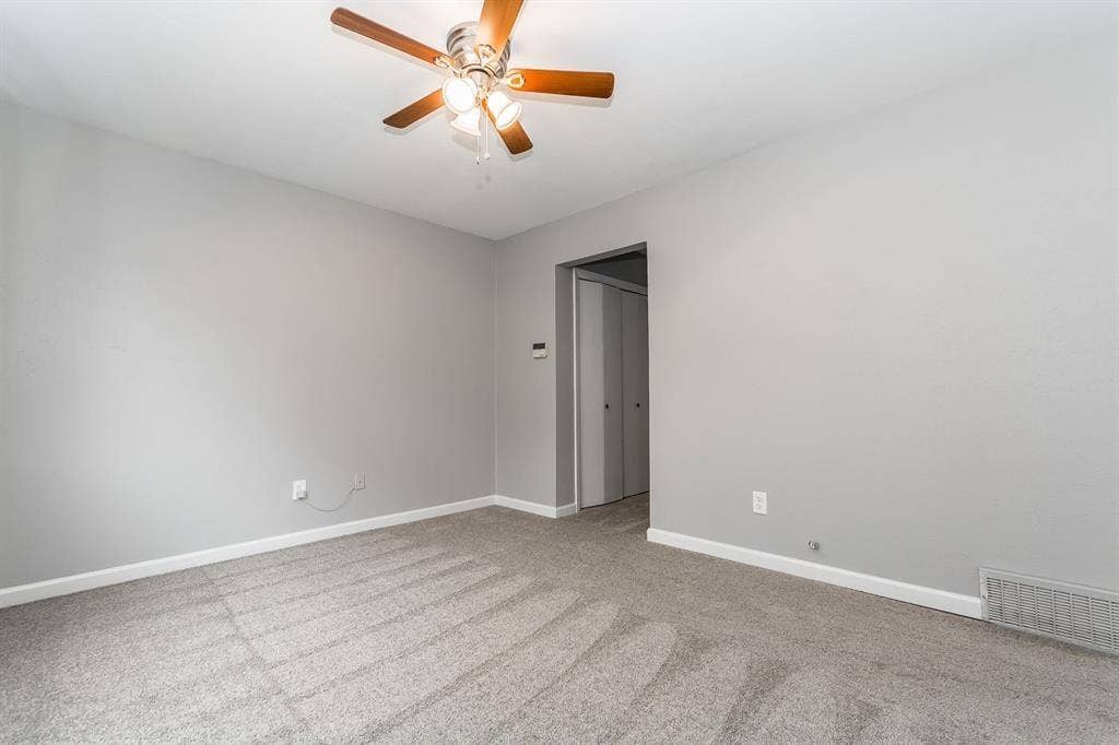 Neutral-toned interior room featuring wall-to-wall carpeting and a ceiling fan with integrated light fixtures