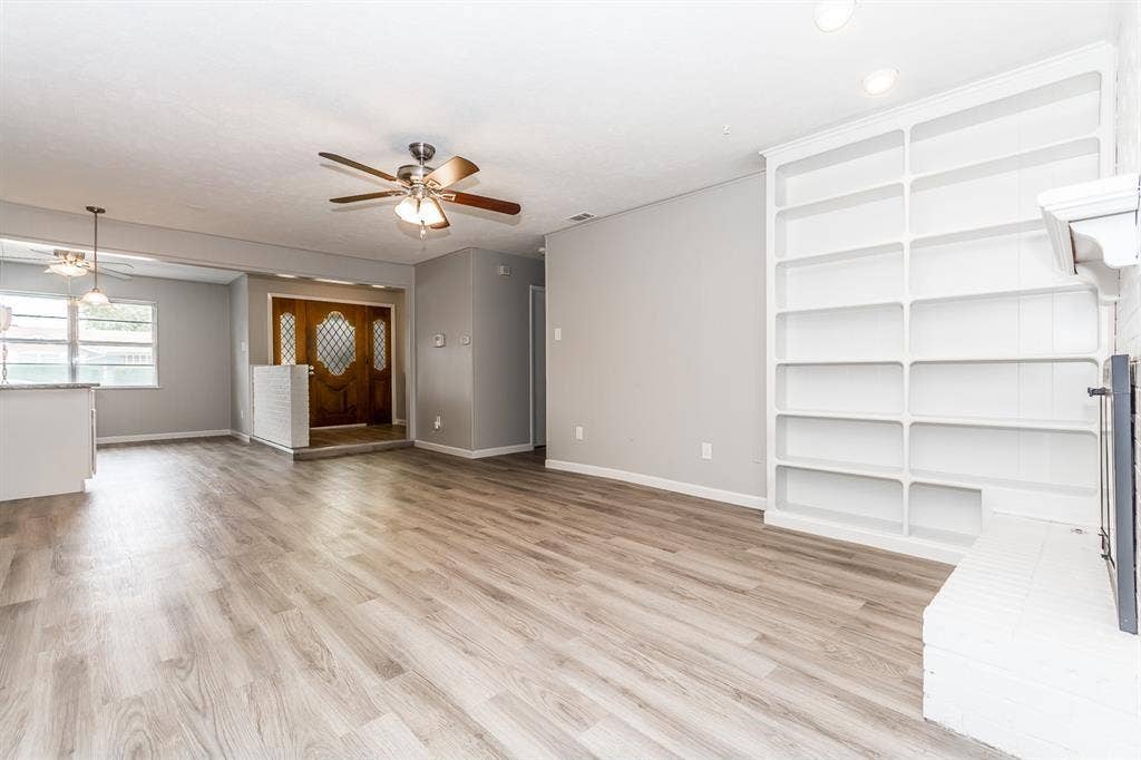 Open concept room featuring wood-finish flooring, built-in floor-to-ceiling shelving, recessed lighting, ceiling fan, and painted brick fireplace hearth