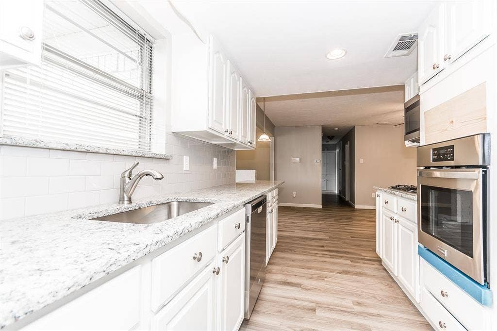 Kitchen featuring white cabinetry, stone-finish countertops, stainless steel wall-mounted oven, subway tile backsplash, and wood-finish flooring