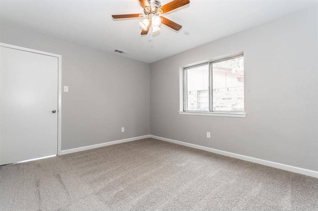 Neutral-toned interior space featuring wall-to-wall carpeting, a multi-blade ceiling fan with integrated lighting, and a dual-pane sliding window