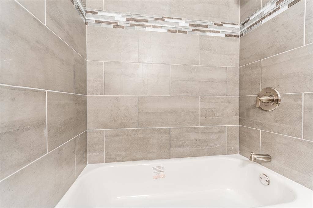 Bathtub surround featuring large-format ceramic tile, a decorative mosaic glass tile accent border, and brushed nickel hardware