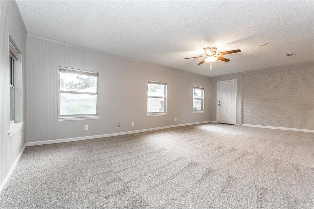 Neutral-toned interior featuring vertical paneled wall treatments, a painted brick accent wall, carpeted flooring, and a ceiling-mounted light fixture with fan blades