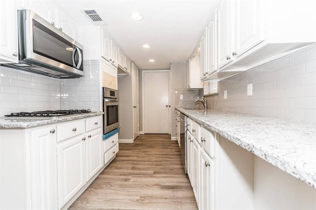 Kitchen featuring white cabinetry, stone-surface countertops, subway tile backsplash, stainless steel appliances, and wood-finish flooring