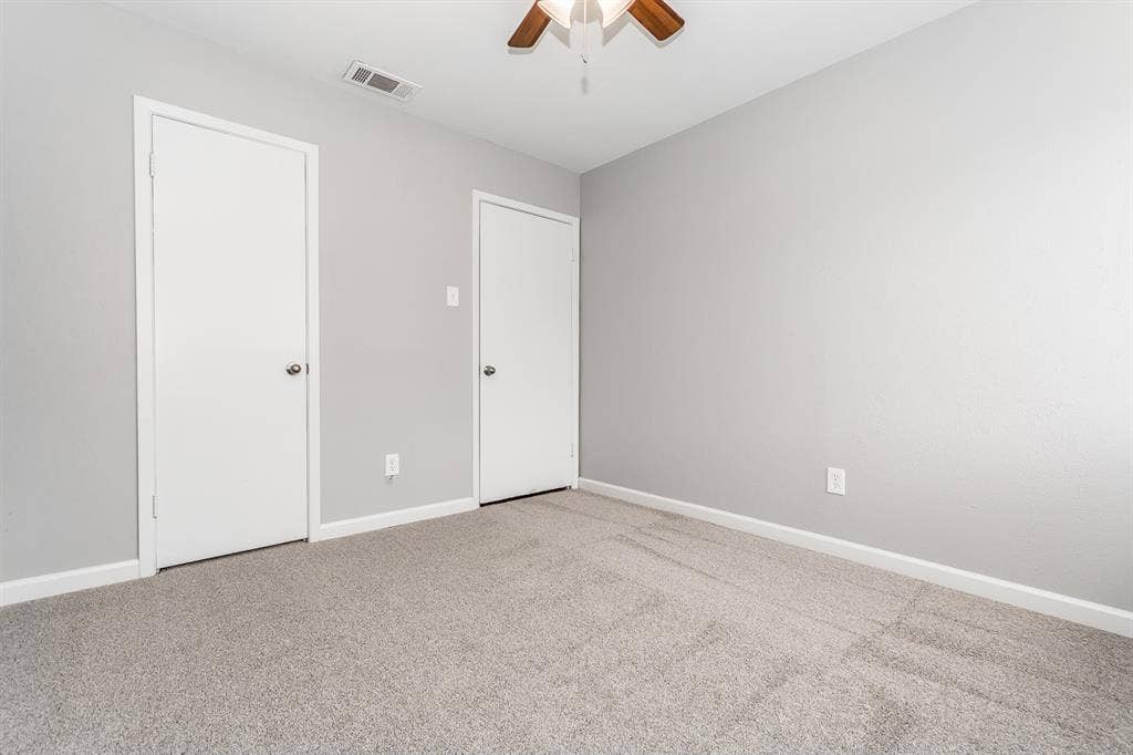 Neutral interior room featuring neutral-toned carpeting, two interior doors, and a ceiling fan with integrated lighting