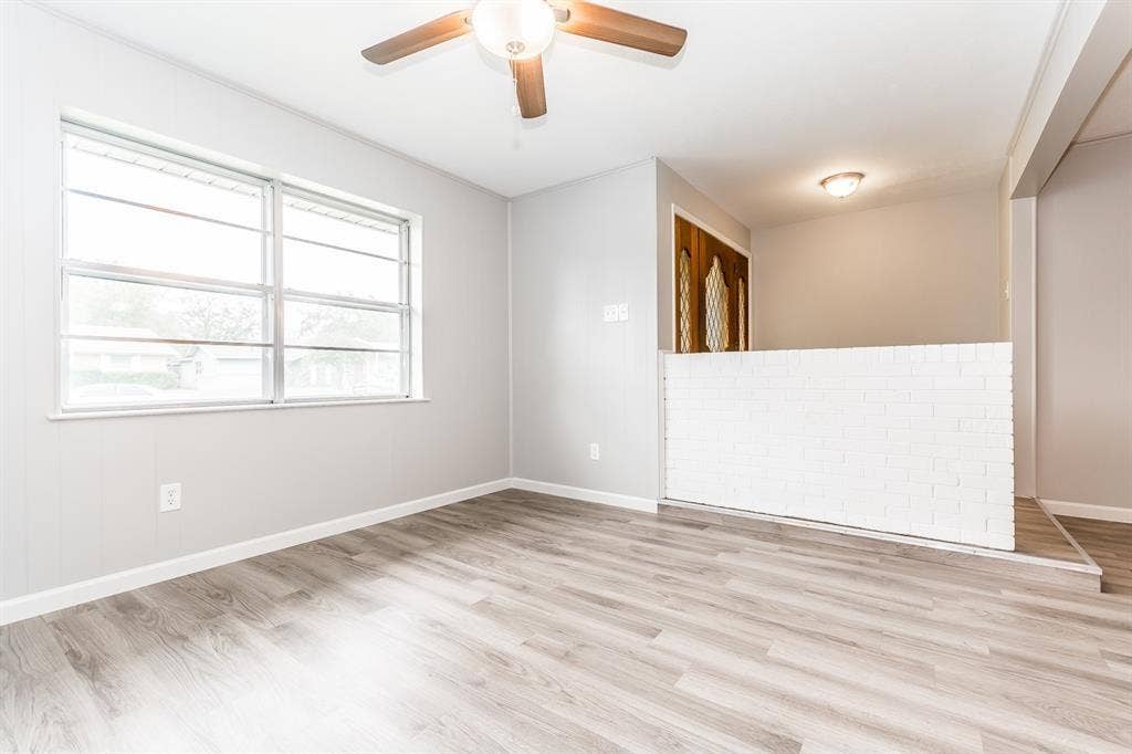 Interior space featuring wood-finish flooring, a painted brick half-wall, large multi-pane windows, and a ceiling fan with integrated lighting