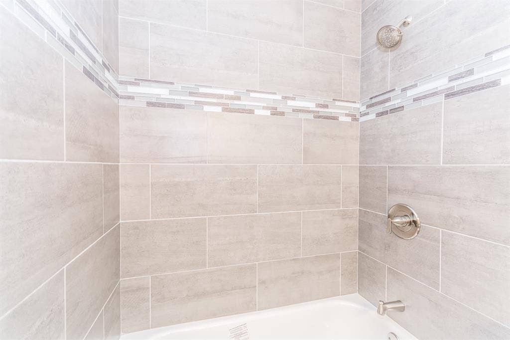 Shower surround featuring large-format neutral-toned tile, decorative glass mosaic accent inlay, polished chrome single-handle pressure balance valve, and a wall-mounted shower head