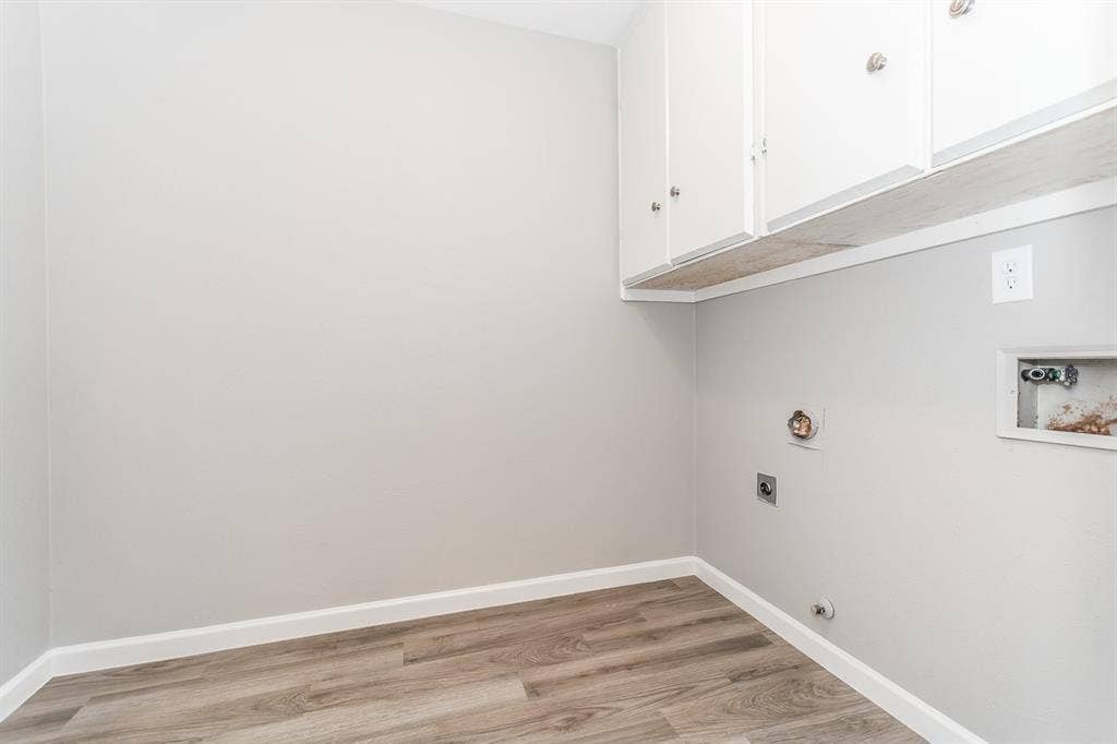 Utility space featuring wood-finish flooring, white wall-mounted upper cabinetry, and dedicated plumbing and electrical hookups