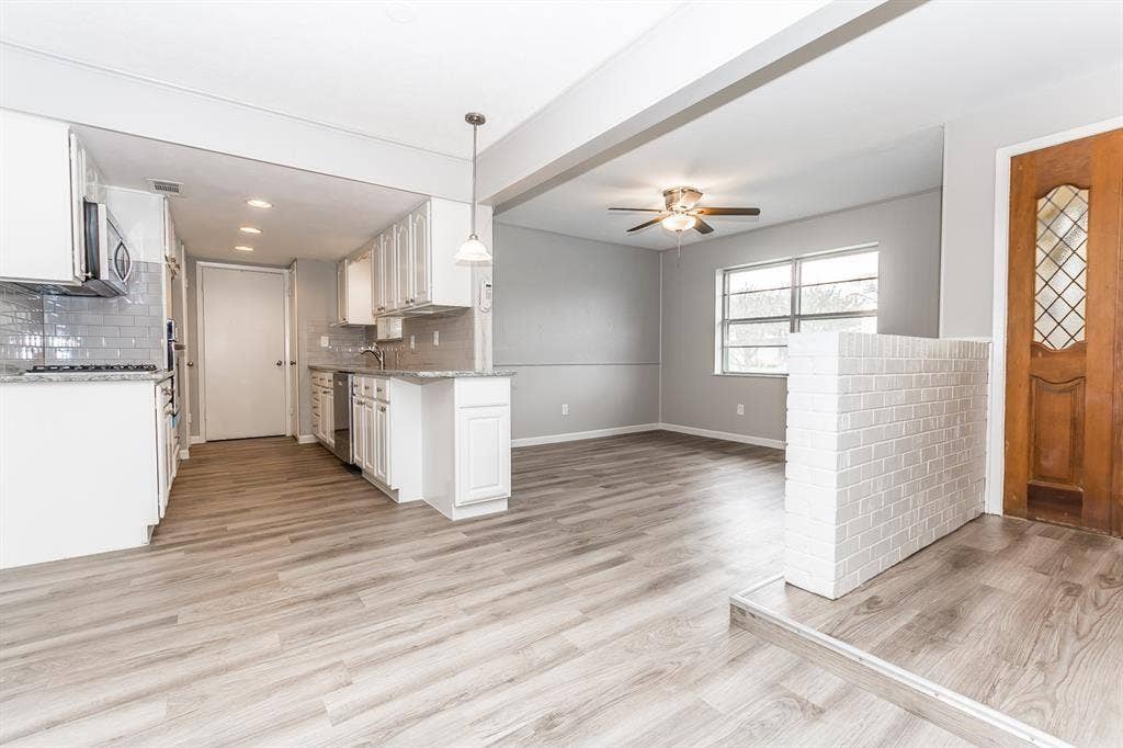 Kitchen featuring white shaker-style cabinetry, stone-surface countertops, subway tile backsplash, wood-finish flooring, and a decorative white brick partial wall