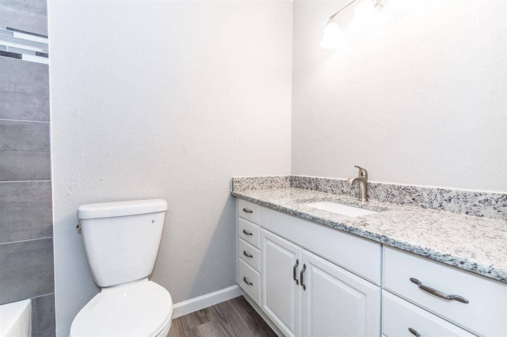 Bathroom vanity featuring white cabinetry, stone-finish countertop, undermount sink, brushed nickel hardware, and wood-finish flooring