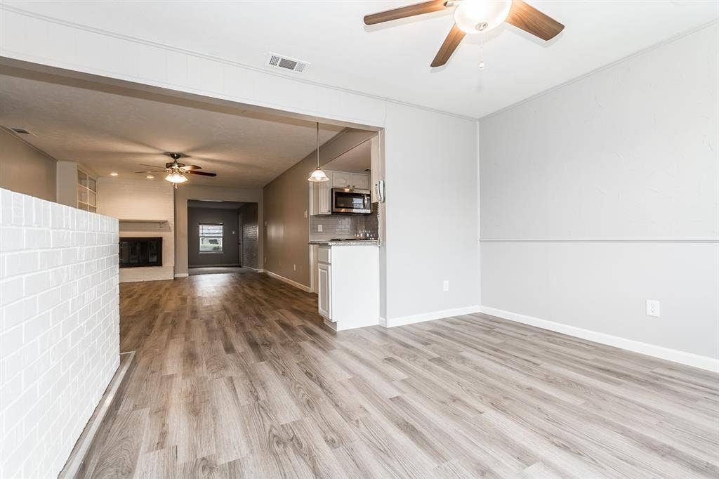 Wood-finish flooring throughout, white painted brick partition, ceiling fan with integrated lighting, kitchen featuring built-in cabinetry, and built-in fireplace