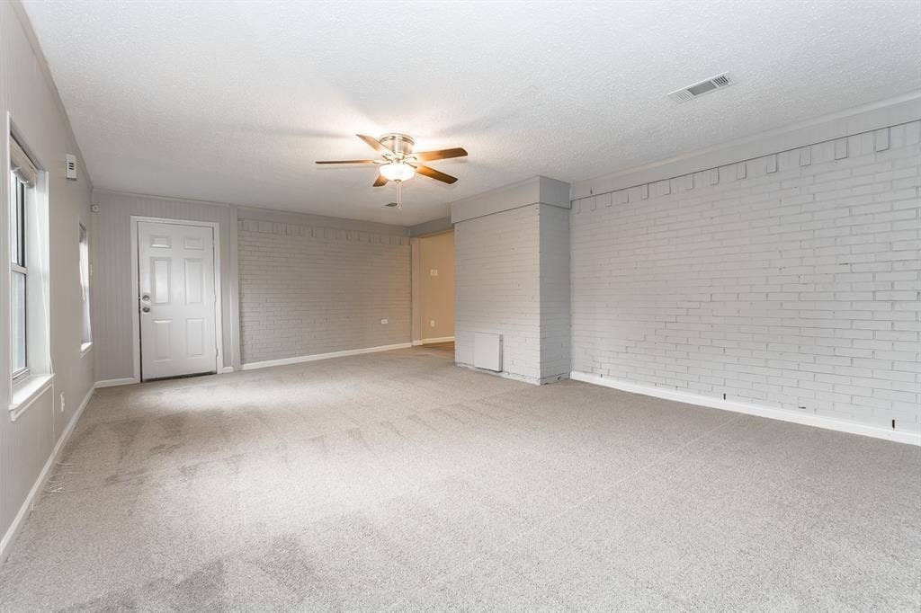 Spacious interior featuring painted brick wall accents, wall-to-wall carpeting, and a ceiling fan with integrated lighting