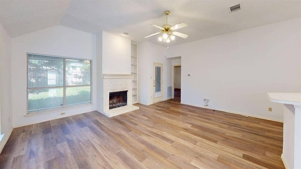 733 Rockett Lane, Cedar Hill, TX 75104 Living area featuring vaulted ceilings, wood-finish flooring, a painted brick fireplace, built-in shelving, and a ceiling fan with integrated lighting