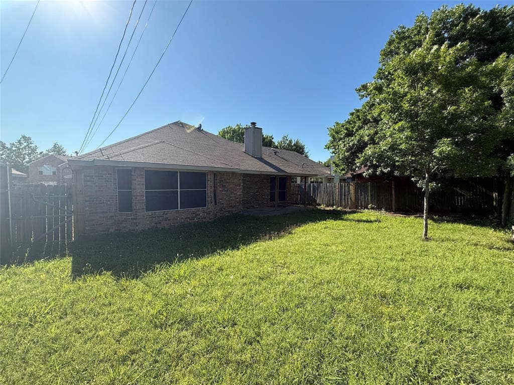 733 Rockett Lane, Cedar Hill, TX 75104 Exterior backyard featuring brick masonry, a central chimney, mature trees, and perimeter wood fencing