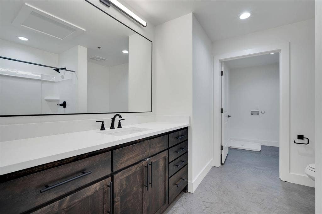 301 W Main Street, #252, Midlothian, TX 76065 Bathroom featuring custom dark-wood cabinetry, white solid-surface countertop, matte black fixtures, full-width mirror with integrated lighting, and polished concrete flooring