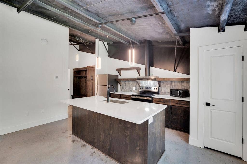 301 W Main Street, #252, Midlothian, TX 76065 Industrial-style kitchen featuring an exposed concrete ceiling, dark wood-finish cabinetry, quartz countertops, a central island with an integrated sink, and cylinder pendant lighting
