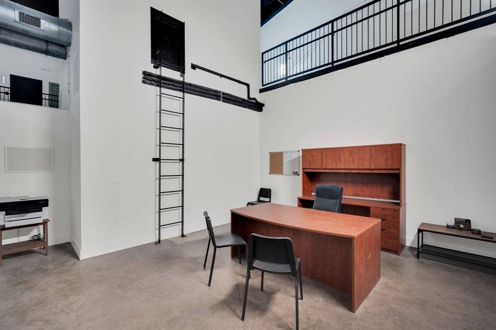 Industrial-style interior featuring soaring ceilings, concrete flooring, a fixed metal ladder, and a railed mezzanine level