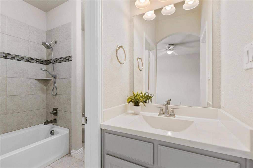 4109 Rainey Street, McKinney, TX 75070 Bathroom featuring a vanity with a white countertop and integrated sink, a large wall-mounted mirror, a tub-shower combination with decorative tile inlay, and polished metal hardware